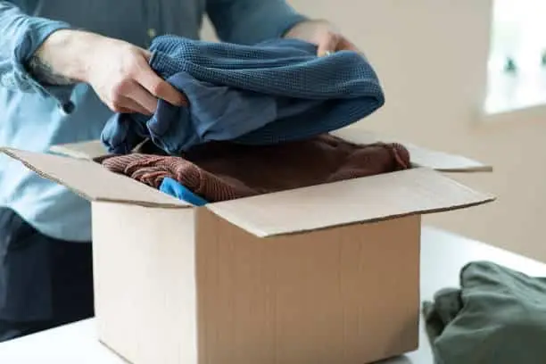 Person placing folded clothing into a cardboard donation box
